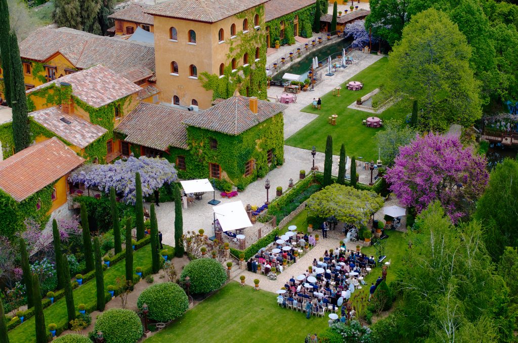Vista aérea de una ceremonia de boda al aire libre en una finca de Madrid, con sillas para los invitados, un altar y un edificio principal con piscina.