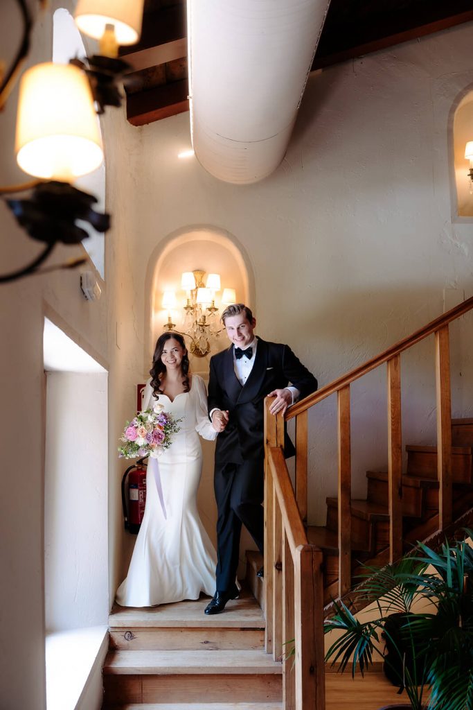 Novios Barna y Natalia bajando la escalera de la Antigua Fábrica de Harinas después de la ceremonia. La novia viste un traje de manga larga y lleva un ramo de flores.