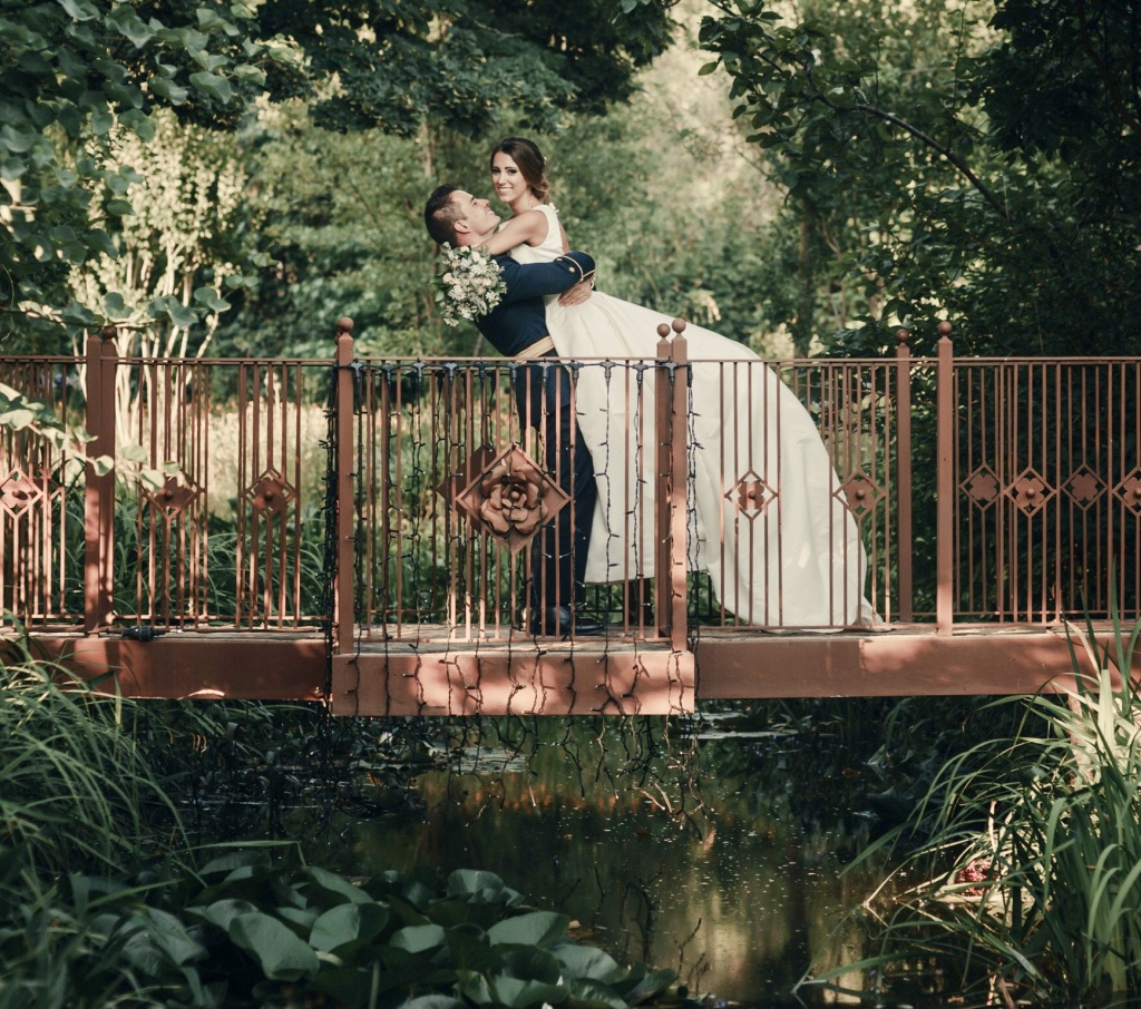 Planificación de boda: escena en puente de jardín Personas con traje de boda sobre un puente en un jardín, ilustrando la planificación de boda paso a paso de 12 a 0 meses.